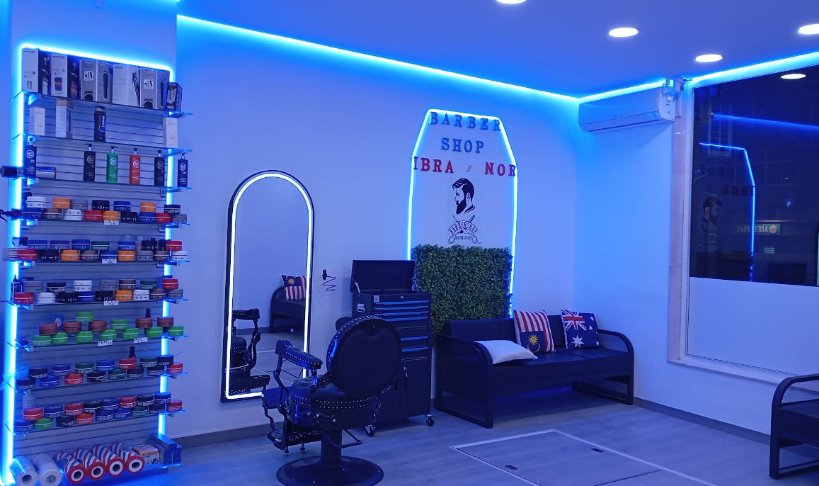 Interior de Ibra & Nor con luz azul, el letrero Barber Shop Ibra & Nor, un espejo y un sofá.